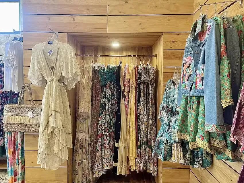 Innenraum des Geschäfts Cocco & Cocó mit Boho-Kleidern auf Kleiderbügeln vor Holzwänden