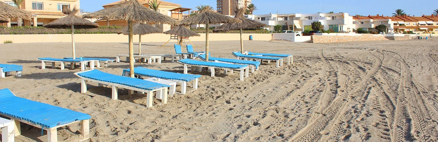 Transats bleus alignés sous des parasols de paille sur le sable ratissé de Playa Galúa