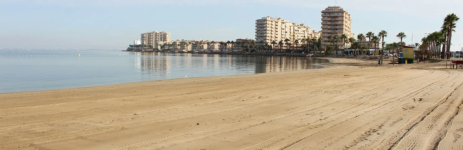 Raked sand at Playa Mistral, with the breakwater and buildings of La Manga in the background