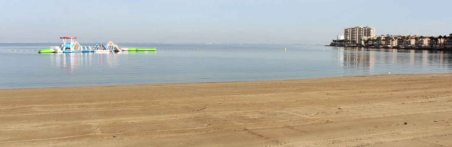 Playa Mistral with inflatable attractions on the flat waters of Mar Menor and buildings of La Manga in the background