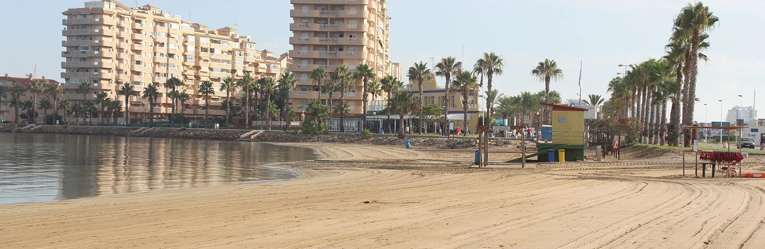 Sand at Playa Mistral, with palms, service huts and swimmers beside the calm waters of Mar Menor