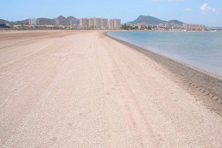 Heller, breiter Sandstrand von Playa Paraíso am Mar Menor, mit dem Gebirge und den Gebäuden im Hintergrund