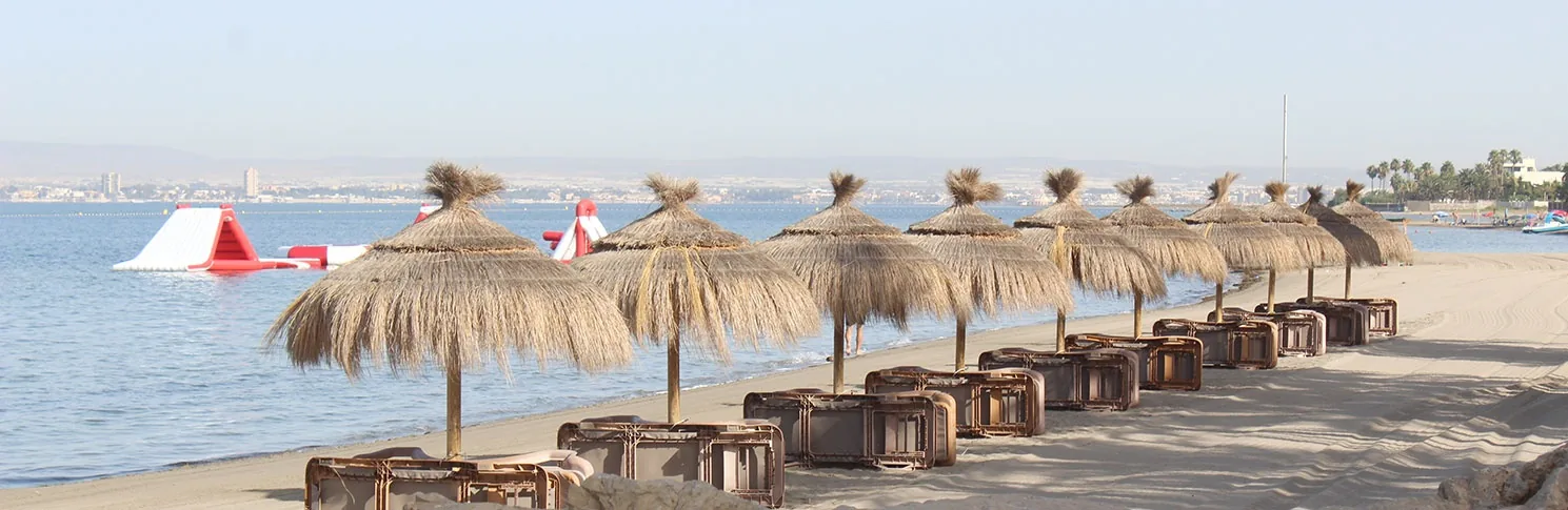 Strohschirme und Holzliegen auf dem Sand der Playa La Veneziola, am ruhigen Mar Menor