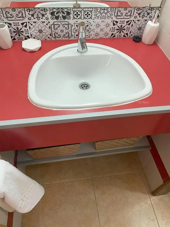 Apartment bathroom basin with a red worktop and patterned tiles