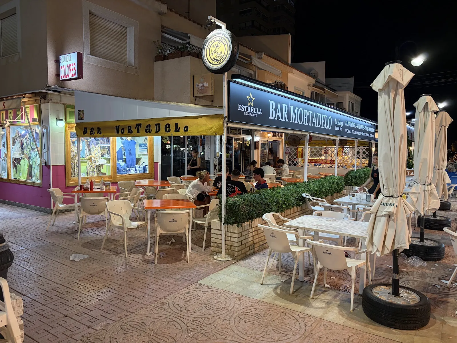 Façade illuminée du Bar Mortadelo la nuit, avec des clients en terrasse