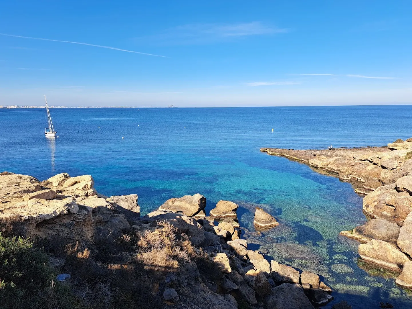 Rocky cove with clear water and a sailing boat, in Cabo de Palos
