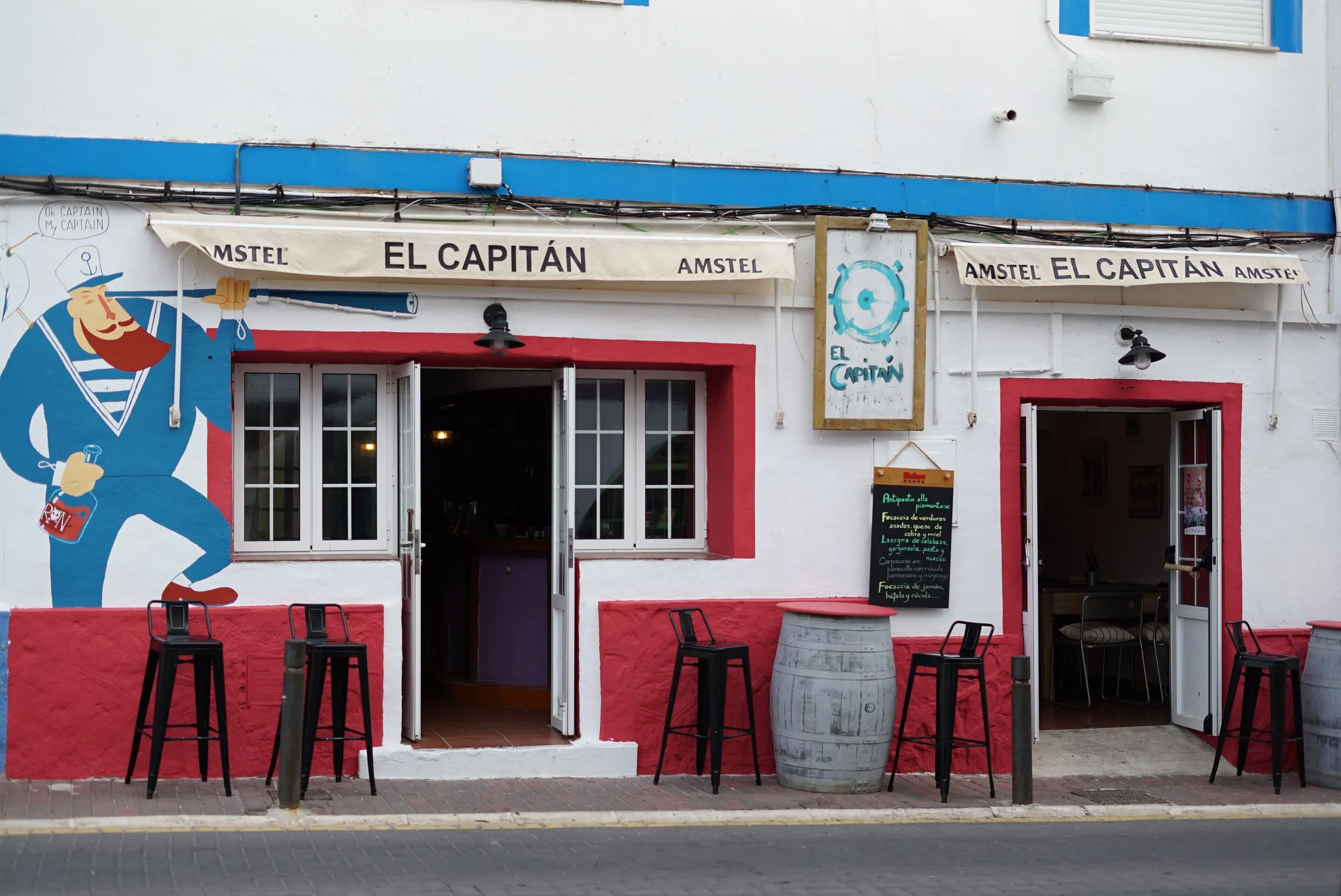 Front of El Capitán on Calle Marín, Cabo de Palos, with a ship's captain mural and a terrace with stools