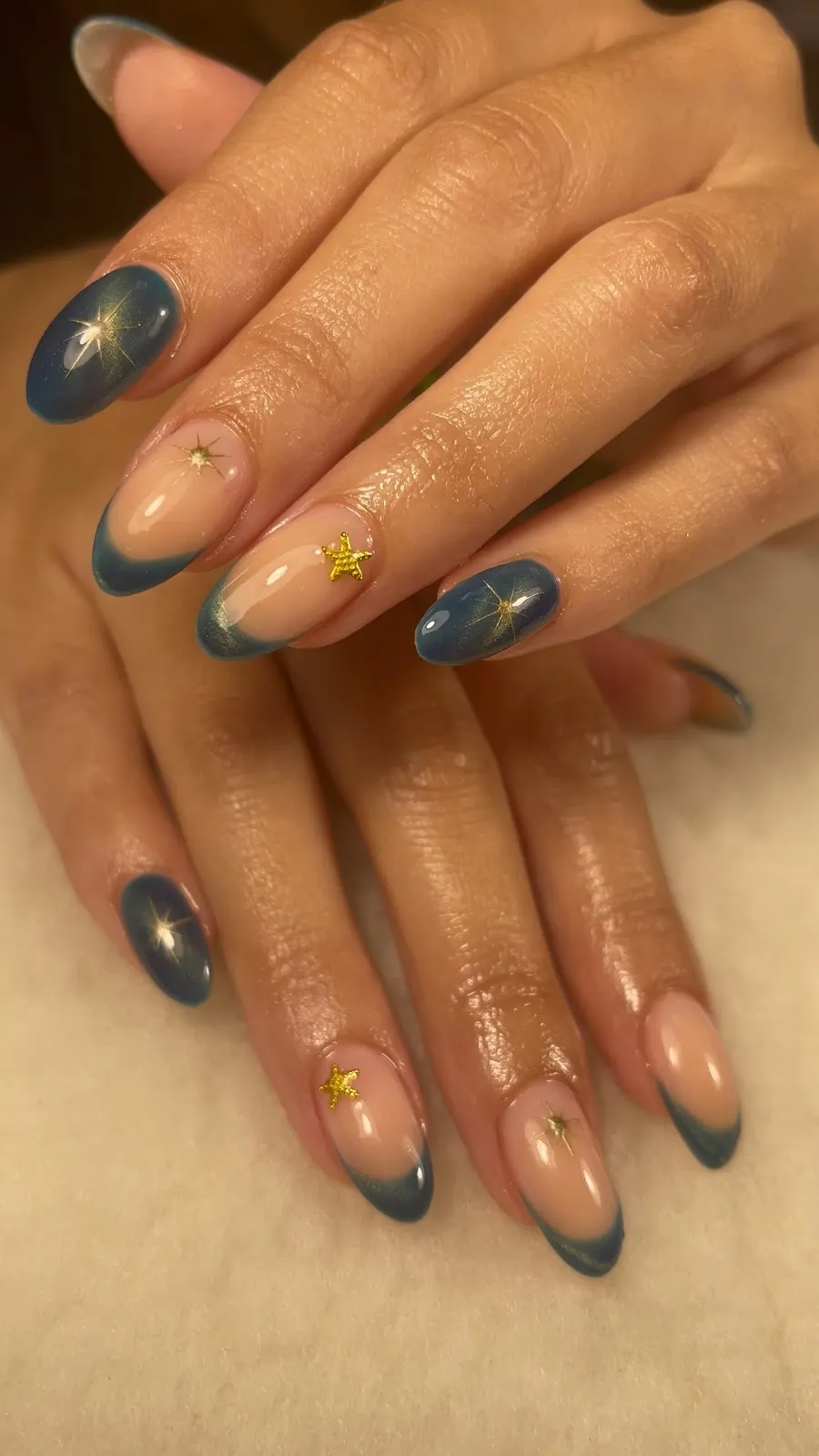 Blue galaxy-effect manicure with gold star details, Estética Angy de Béjar