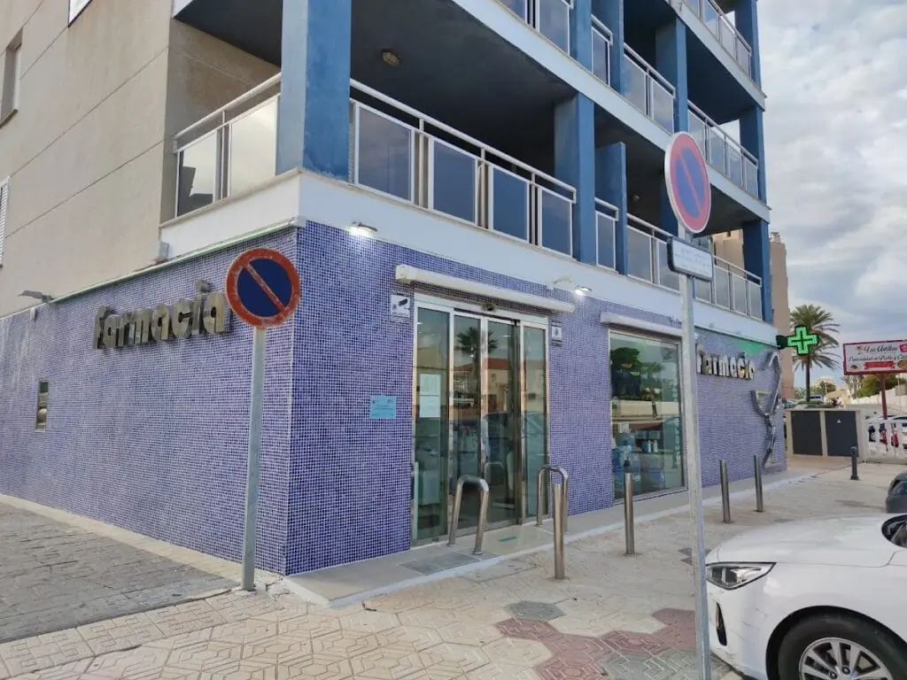 Front of Farmacia La Manga Centro, with blue tiles and a Farmacia sign with a green cross, km 8 Gran Via de la Manga