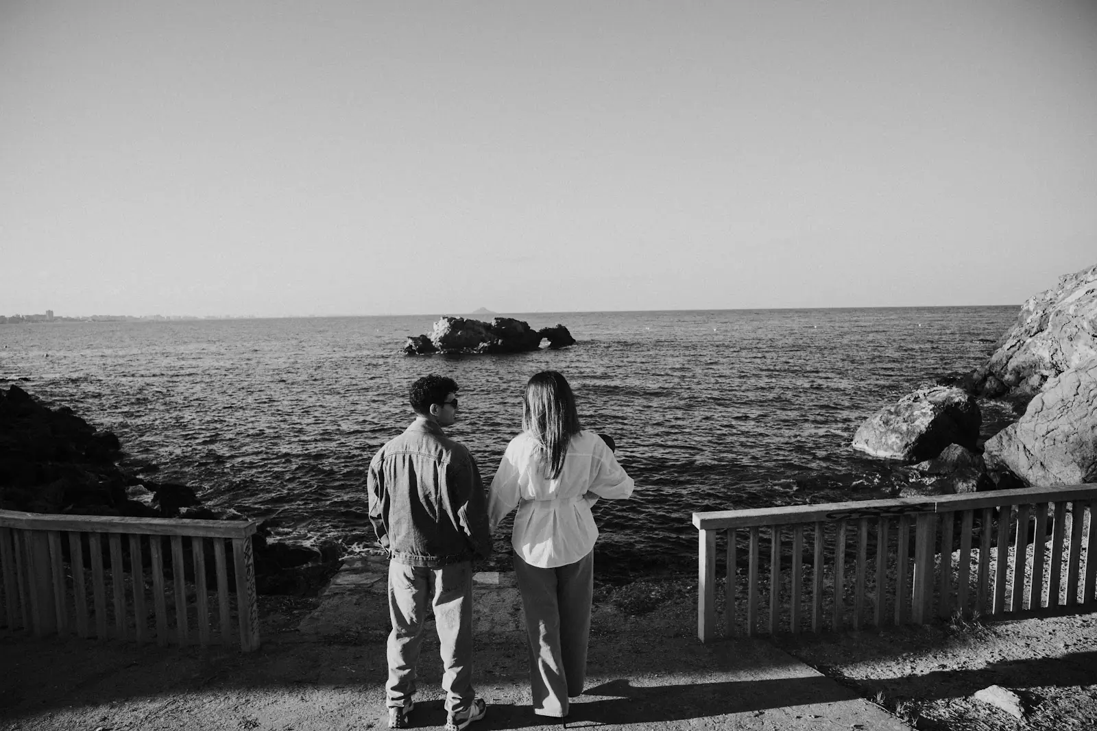 Black-and-white photograph of a couple looking out to sea beside rocks, by José Espinosa