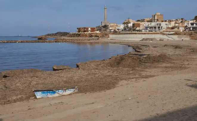 Plage avec une barque échouée et le phare de Cabo de Palos au fond