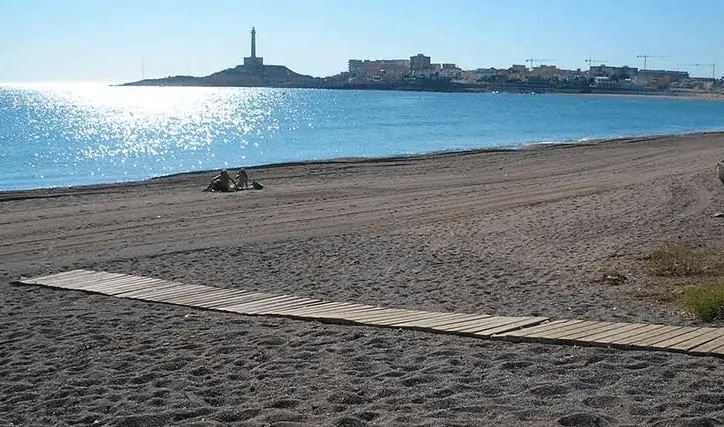 Plage de sable avec une passerelle et le phare de Cabo de Palos au fond