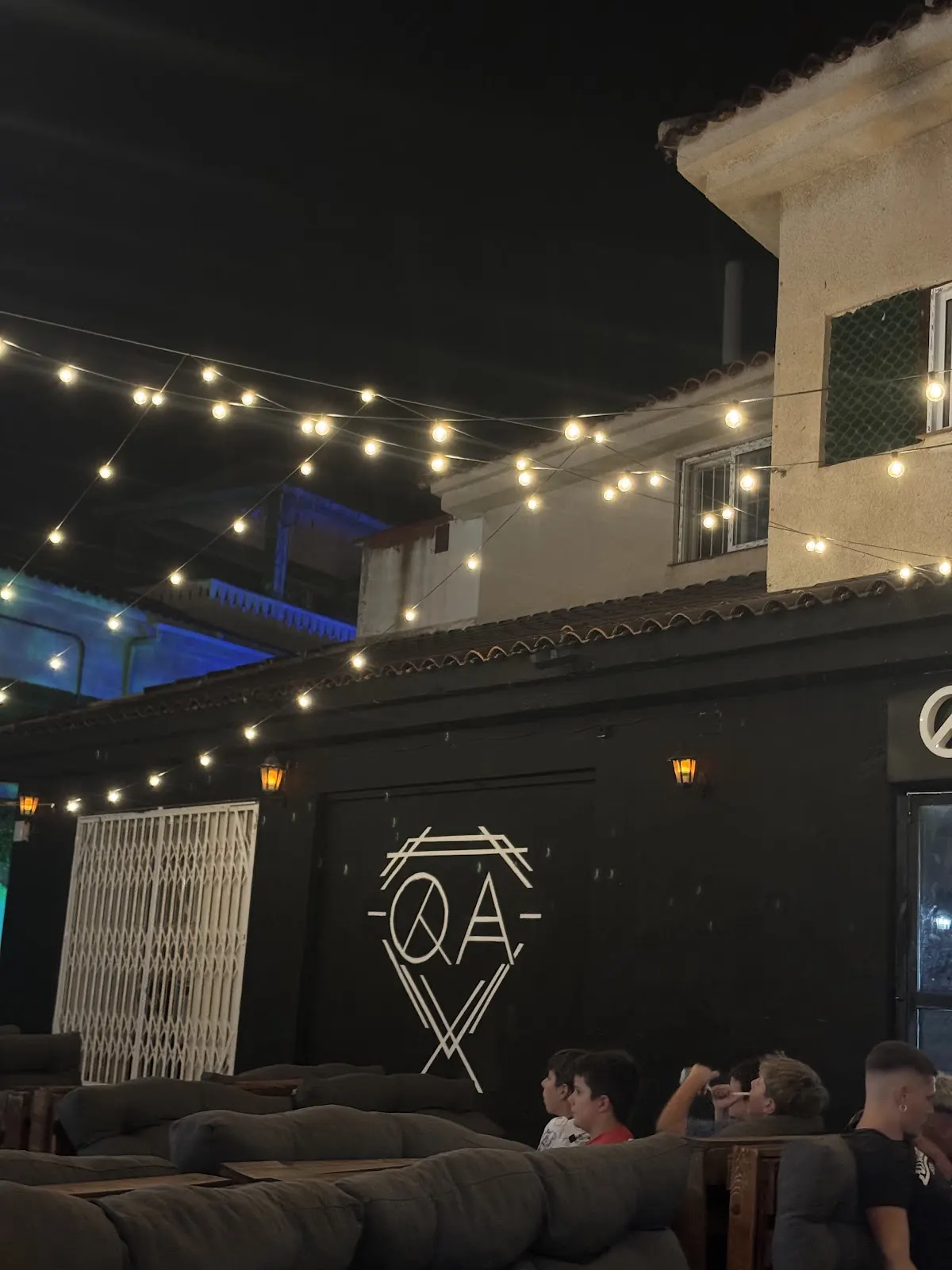 Fassade von Quality Pub bei Nacht mit Lichterketten und dem QA-Logo