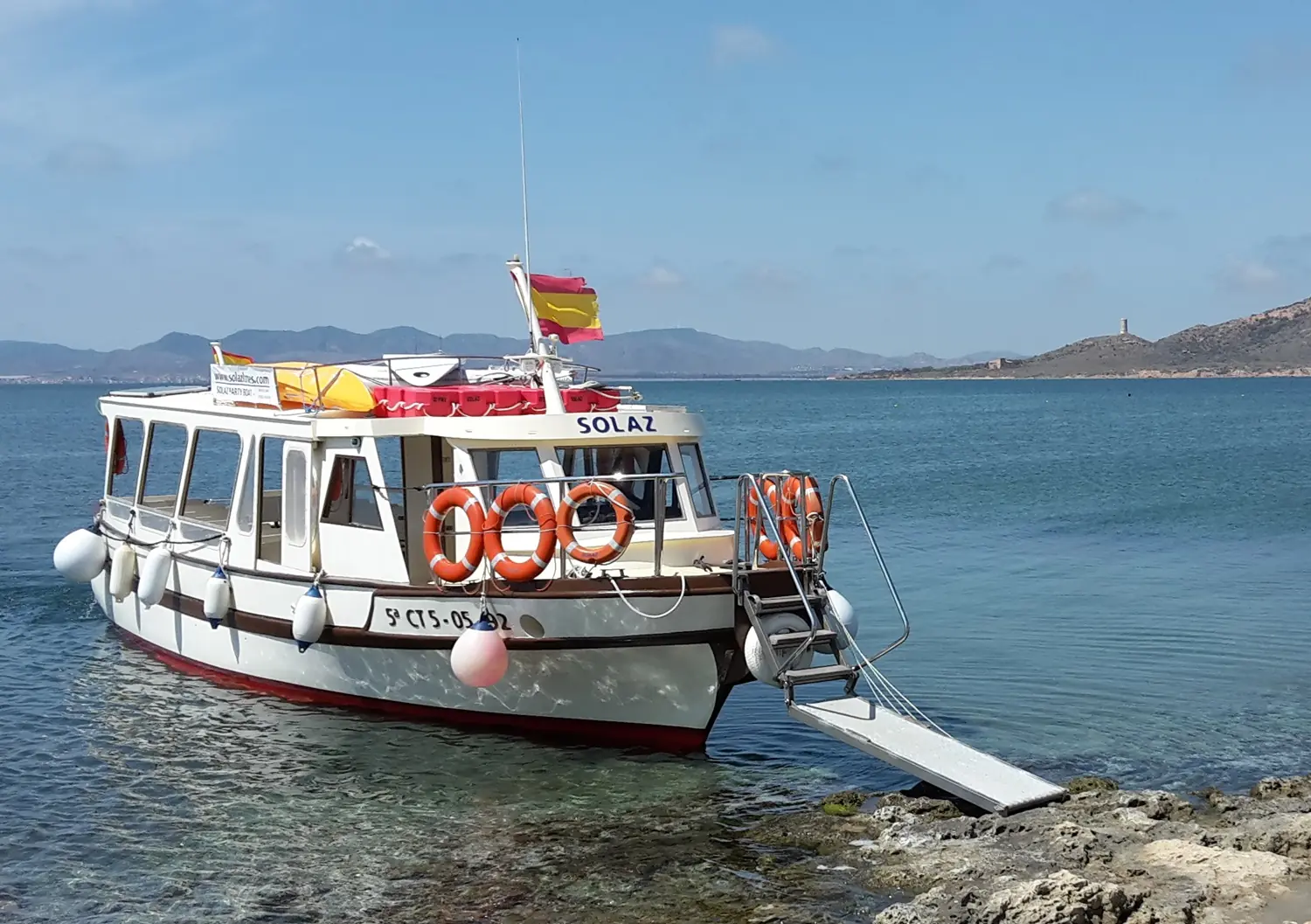 Das Boot Solaz liegt mit ausgefahrenem Steg an der felsigen Küste der Isla Grosa