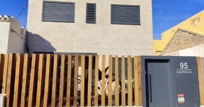 Fachada exterior de 95 Lighthouse en Playa de Levante, villa moderna con valla de listones de madera y puerta gris numerada