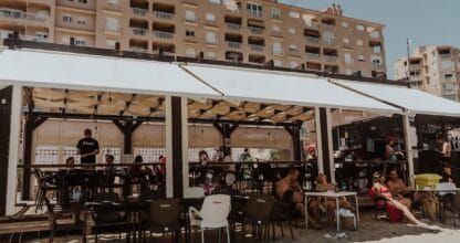 Chiringuito A Tu Aire en La Manga del Mar Menor con terraza bajo toldo blanco llena de clientes en bañador y barra de bar al fondo