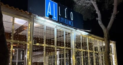 Fachada nocturna del restaurante Al Lío Experience decorada con luces de hada doradas y gran estructura acristalada