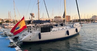 Velero blanco de la Escuela Náutica Ortega amarrado al atardecer en el puerto de La Manga del Mar Menor con bandera española