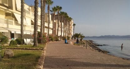 Paseo marítimo con palmeras junto al Mar Menor frente a Apartamentos El Pedruchillo con vistas a la sierra al fondo