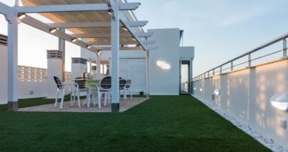 Terraza ático de Apartamentos Maria Guerrero con césped artificial, pérgola blanca y mesa de comedor exterior al atardecer
