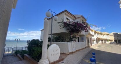 Edificio de apartamentos Cabo Romano frente al Mar Menor, fachada blanca con buganvilla rosa y piedra con el nombre del complejo en primer plano