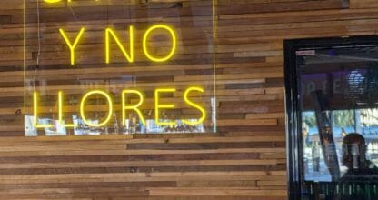 Cartel de neón amarillo con el lema Canta y No Llores sobre pared de madera en el restaurante Aroma de México