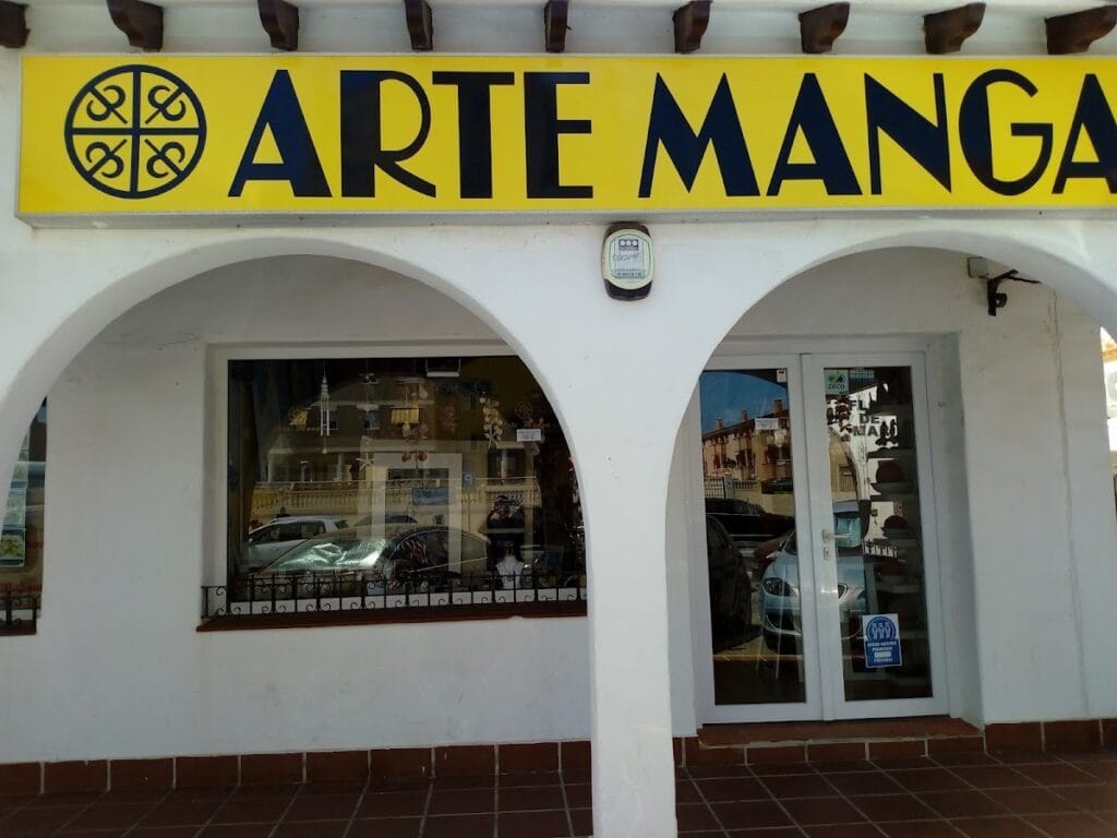 Fachada de tienda Arte Manga con gran rótulo amarillo y negro sobre edificio blanco de arcos en La Manga del Mar Menor