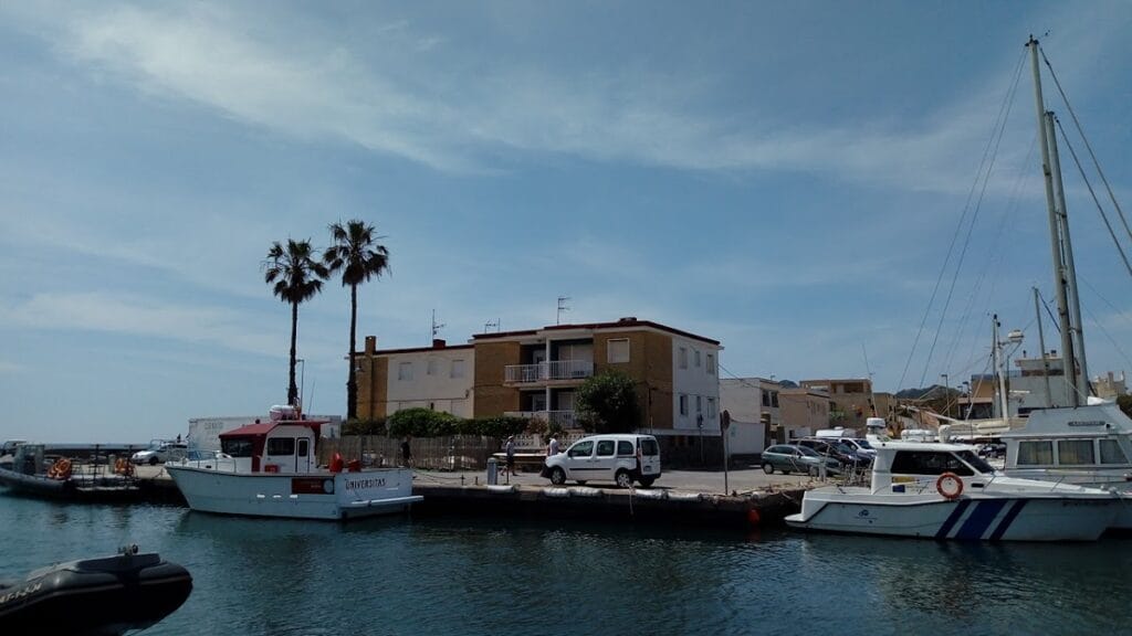 Puerto pesquero de Cabo de Palos con barcos amarrados, velero y edificios residenciales junto al mar