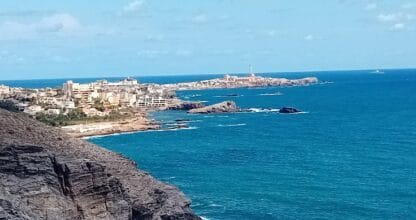 Vista panorámica del litoral rocoso con el pueblo y faro de Cabo de Palos al fondo, desde Avatel