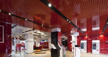 Interior de sucursal Banco Santander Agentes con techo rojo perforado, cajeros automáticos y zona de información