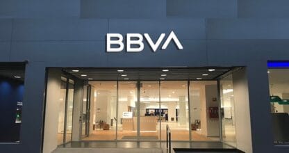 Fachada moderna de oficina bancaria BBVA de noche con gran rótulo luminoso blanco y acceso acristalado iluminado