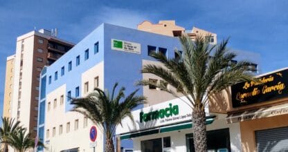 Edificio azul de la Biblioteca La Manga del Mar Menor con palmeras y farmacia en planta baja