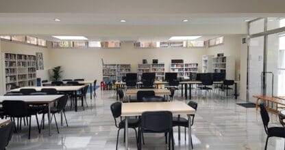 Interior de la Biblioteca de La Manga del Mar Menor con mesas de estudio, sillas negras, estanterías y ordenadores