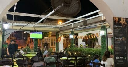 Terraza nocturna de Brasería La Vaca Gallega con mesas verdes, clientes cenando y televisión en La Manga