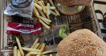 Dos hamburguesas con sesame bun y patatas fritas servidas en bandeja con papel de periódico en Burger Pay Pay, La Manga