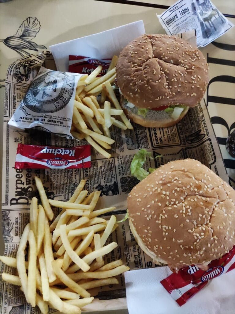 Dos hamburguesas con sesame bun y patatas fritas servidas en bandeja con papel de periódico en Burger Pay Pay, La Manga