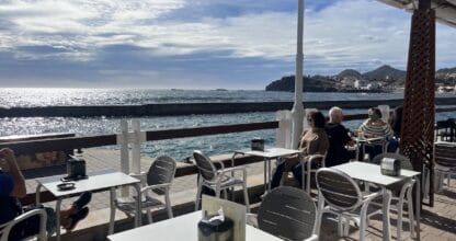 Terraza de Busquets Cafetería-Heladería en Cabo de Palos con clientes sentados frente al mar mediterráneo y vistas al Cabo de Palos al fondo