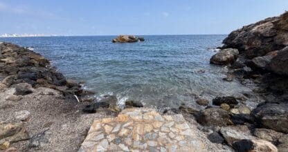 Cala rocosa con aguas azules y transparentes y acceso de piedra en Cala de la Galera, Cabo de Palos