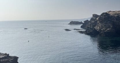 Cala del Clavo con agua turquesa transparente entre formaciones rocosas oscuras en Cabo de Palos, paisaje mediterráneo árido y cielo despejado