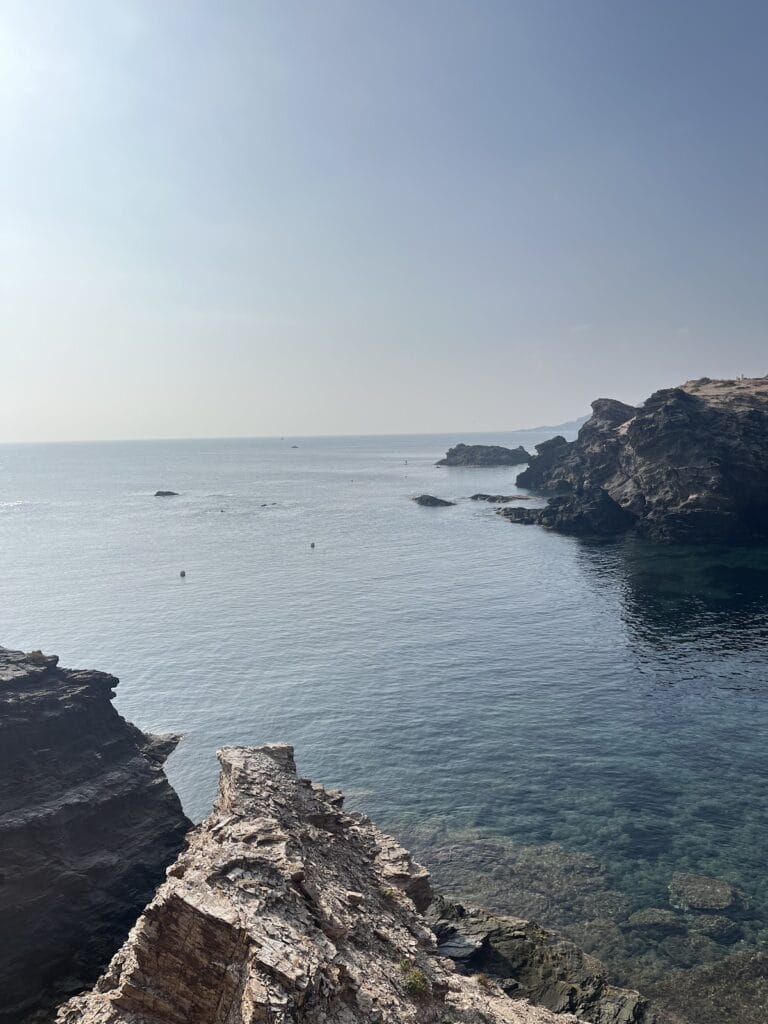Cala del Clavo con agua turquesa transparente entre formaciones rocosas oscuras en Cabo de Palos, paisaje mediterráneo árido y cielo despejado