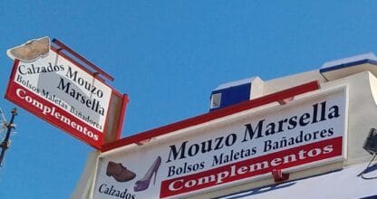 Rótulos de Calzados Mouzo Marsella en La Manga del Mar Menor anunciando calzados, bolsos, maletas, bañadores y complementos bajo cielo azul