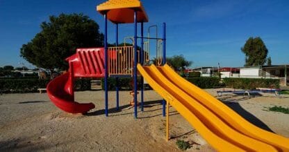 Zona de juegos infantil con toboganes amarillos y rojos en área de arena del Camping La Manga del Mar Menor