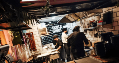 Cocina abierta de Canalla Tacos y Tragos con rótulo Mexican Tapas, cocineros trabajando y barra con copas lista para el servicio