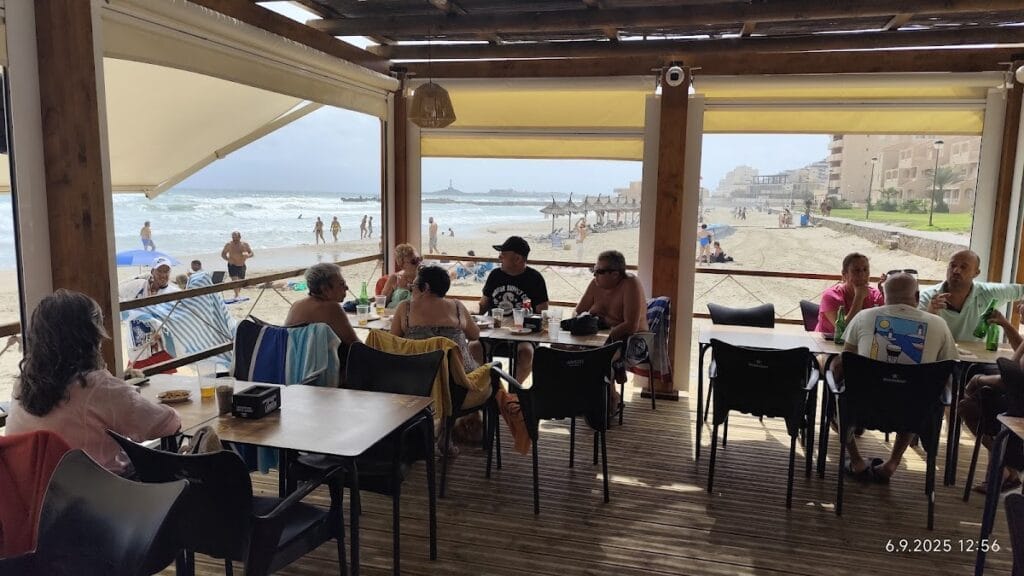 Terraza del Chiringuito 4 Latas con clientes almorzando frente a la playa y el mar agitado en La Manga del Mar Menor