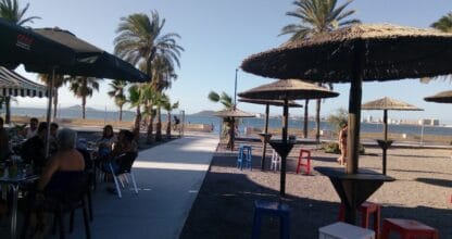 Terraza frente al Mar Menor con sombrillas de paja y clientes en el Chiringuito El Rincón Cubano