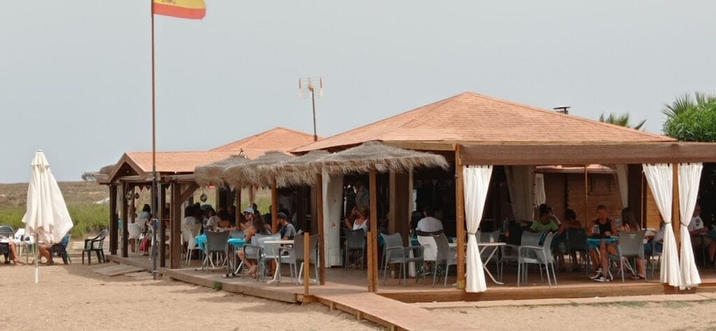 Terraza exterior del Chiringuito Punta de Lomas con mesas llenas de clientes bajo techos de palma y cortinas blancas en La Manga del Mar Menor