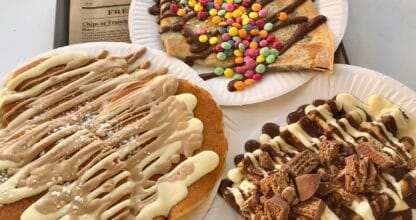 Tres crepes y tortitas dulces de Churreria Mamamia con chocolate, lacasitos, nata y toppings variados servidos en platos de papel sobre bandeja