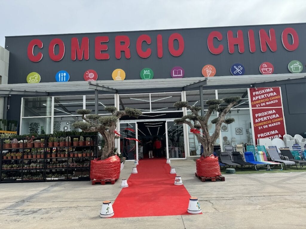Fachada del Comercio Chino La Manga con alfombra roja de inauguración, árboles decorativos y plantas a la entrada