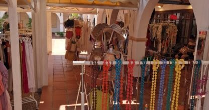 Tienda Cool Spirit en patio exterior con ropa en percheros, collares coloridos y sombreros de paja en La Manga del Mar Menor