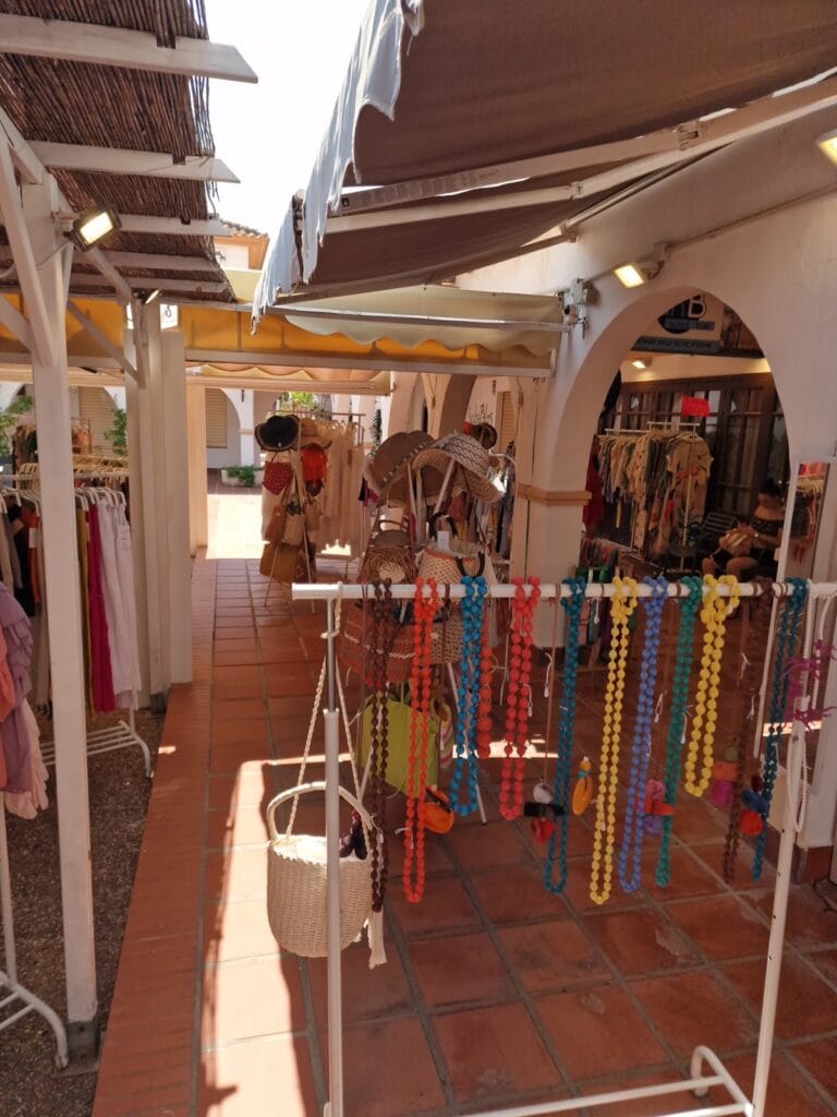 Tienda Cool Spirit en patio exterior con ropa en percheros, collares coloridos y sombreros de paja en La Manga del Mar Menor